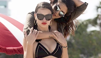 Woman standing behind another woman wearing a bikini and embracing her
