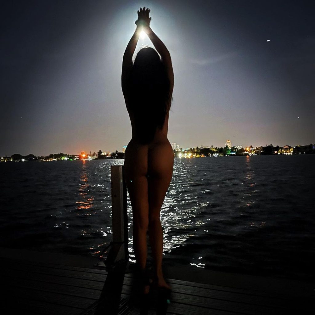 Nude woman showing her backside in front of a lake at night