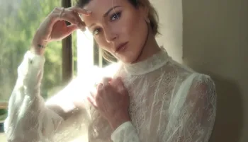 Beautiful blonde sitting in a white dress by a window with sunlight coming in
