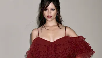 Jenna Ortega in a maroon dress with  a beige background