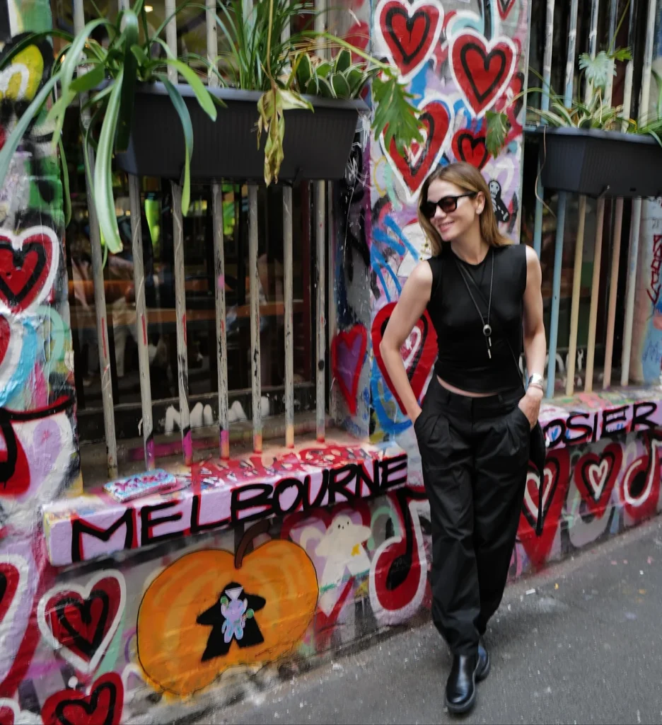Full body view of Michelle Monaghan smiling while posing next to plants and graffiti
