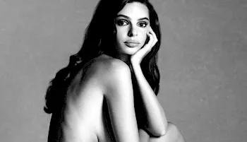Black and white photo of nude woman sitting to her side resting her head in her hand