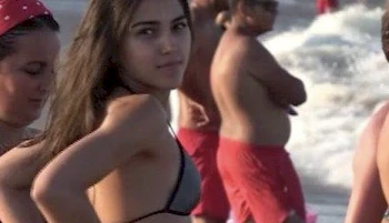 Close up of girl in a bikini at a beach turning around and looking directly into the camera