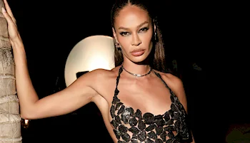 Close up of black model leaning against a palm tree in a sexy dress