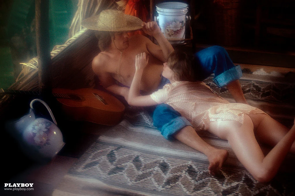 Far away view of Melanie Griffith laying on her stomach on top of a shirtless man