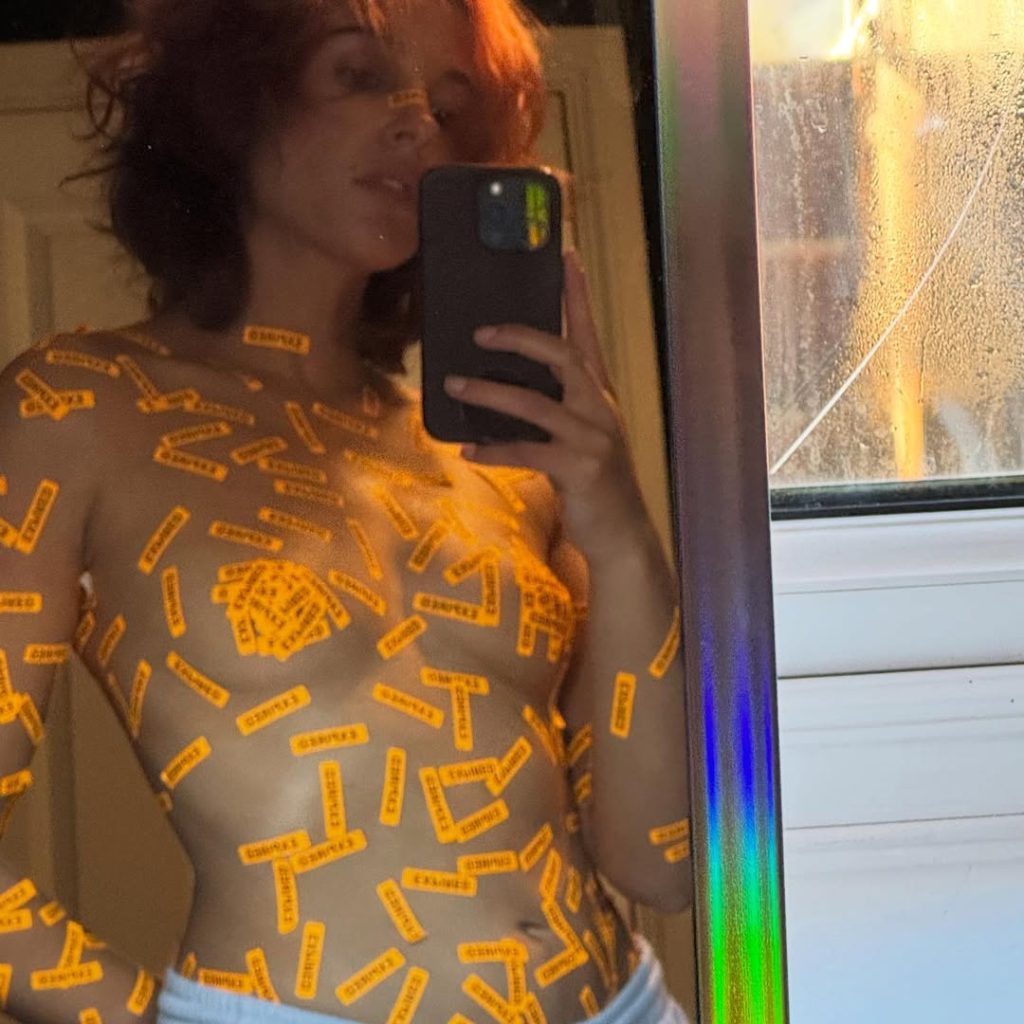 Topless actress wearing small rectangular stickers all over her body taking a selfie