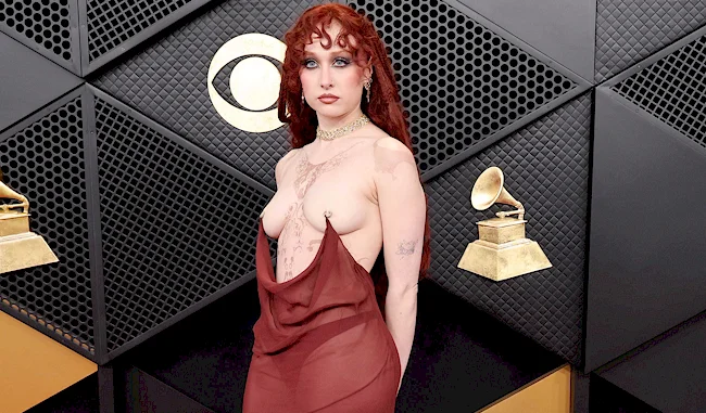 Chappell Roan posing topless with nipple rings and chains on a red carpet