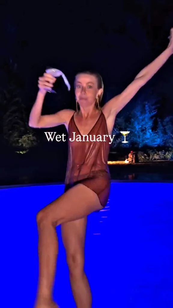 A woman in a sheer, wet outfit stands poolside at night, holding a drink and raising one arm. The text Wet January with a martini glass emoji is overlaid on the image. The pool glows bright blue in the background.