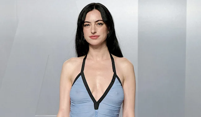 Brunette woman in sheer  blue dress standing in front of a plain background