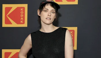 A person wearing a black sleeveless top and a cap poses in front of a backdrop with repeating Kodak logos.