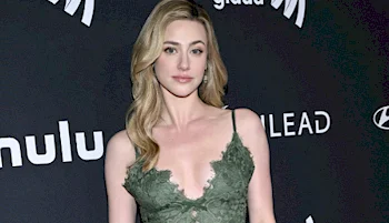 A woman with long blonde hair wearing a green lace dress poses on a black carpet at an event, with logos for Hulu, GLAAD, and Hyundai visible on the backdrop behind her.