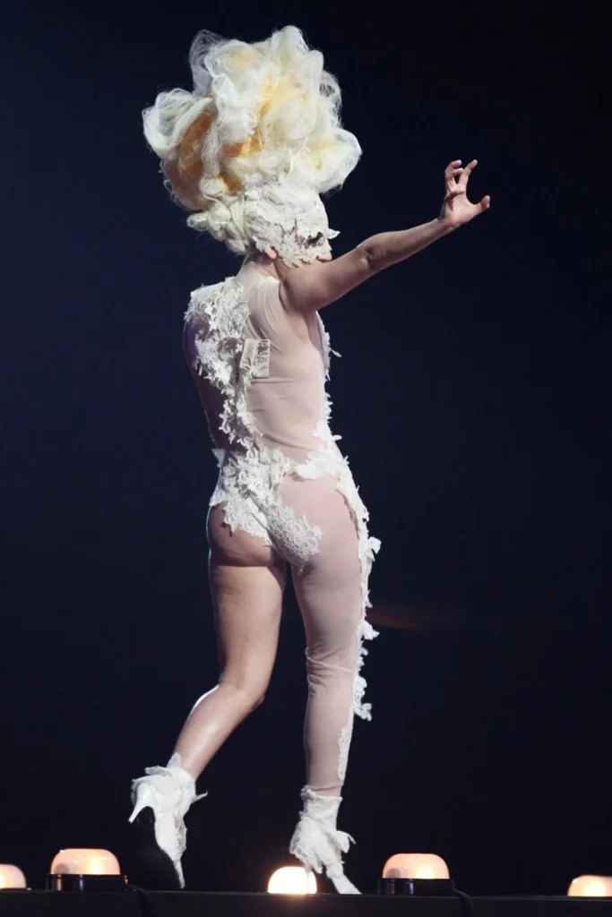 Backside of Lady Gaga in revealing costume walking along a stage and waving at the audience
