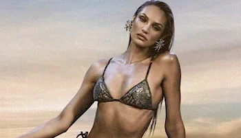 A woman with long hair wears a metallic bikini and large star-shaped earrings, posing outdoors against a sunset sky.