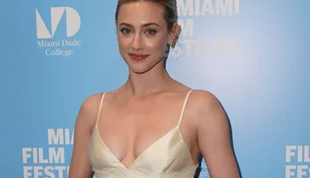 A woman wearing a cream-colored satin dress poses in front of a blue Miami Film Festival backdrop with logos and text for Miami Dade College.
