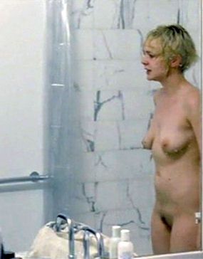 Side view of a naked and wet blonde girl with short hair standing inside a shower