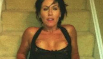 A brunette woman lying on her back on a staircase. Her breasts are out of the top of the dress.