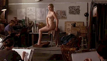 A nude model poses on a platform in an art studio while several artists seated around her sketch or draw. The room is decorated with various artworks and drawing materials.