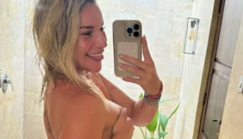 A topless blonde girl is sideways taking a selfie. She smiles and sticks her tongue out.