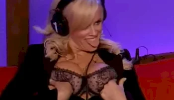 Blonde woman wearing headphones stick her tongue out while grabbing her breasts in a bra.