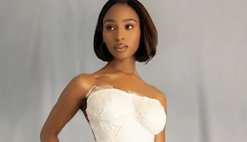 A woman with a bob haircut wears a strapless white top made of plaster and stands against a plain, light gray background.