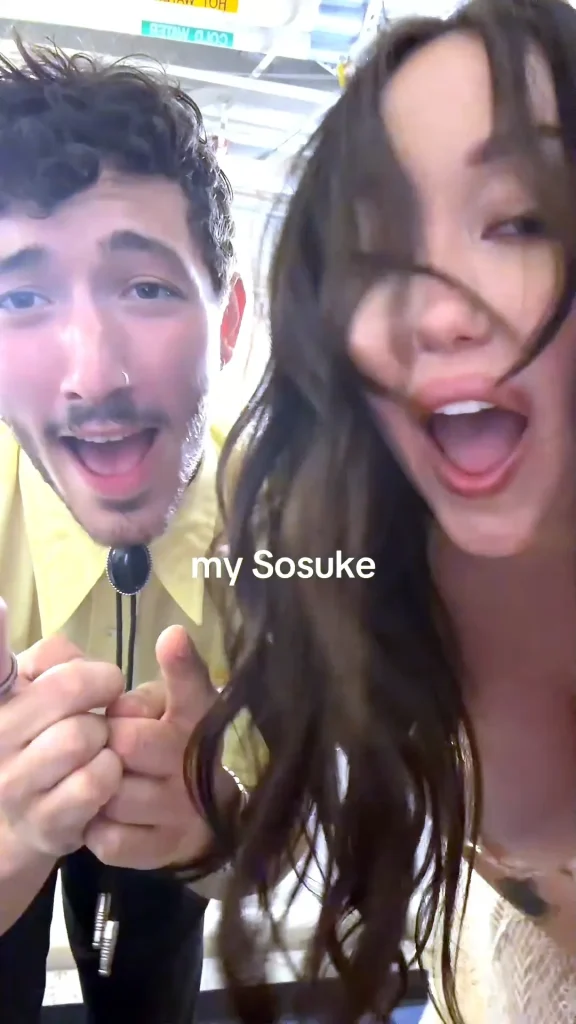 Two young adults smile and pose energetically for the camera; the man wears a yellow shirt and holds a lanyard, while the woman’s hair falls across her face. The text my Sosuke is overlaid on the image.