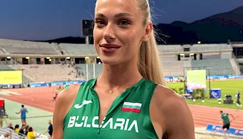 A female athlete in a green Bulgaria uniform stands in a stadium, smiling at the camera. The track and field area and empty stands are visible in the background.