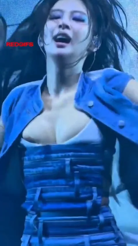A woman in a blue outfit is dancing energetically on stage with her hair flying and eyes closed, mid-performance.