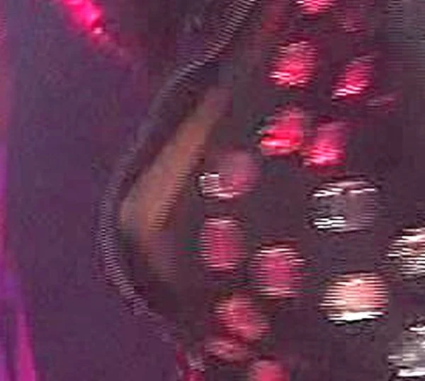 A close-up of a black garment decorated with shiny, reflective sequins in pink and silver hues, with a blurred background containing some purple light.