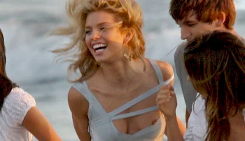 A woman smiling and laughing with friends at the beach, with ocean waves in the background.
