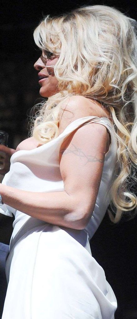 A woman with long, wavy blonde hair wearing a white, sleeveless dress stands in profile, holding a drink.