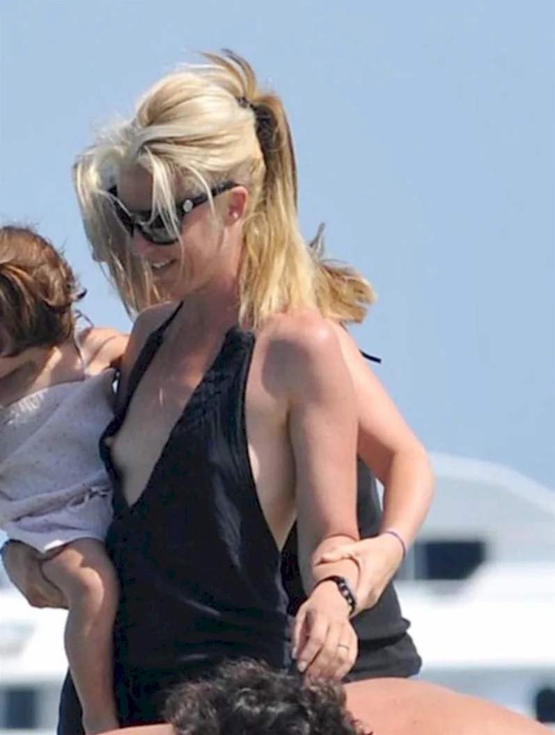 TamaraBeckwithNipSlip2 A woman wearing sunglasses and a black sleeveless top smiles while holding a young child outdoors on a sunny day.