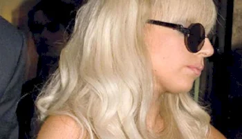 A woman with long, platinum blonde hair, wearing dark sunglasses and facing sideways.