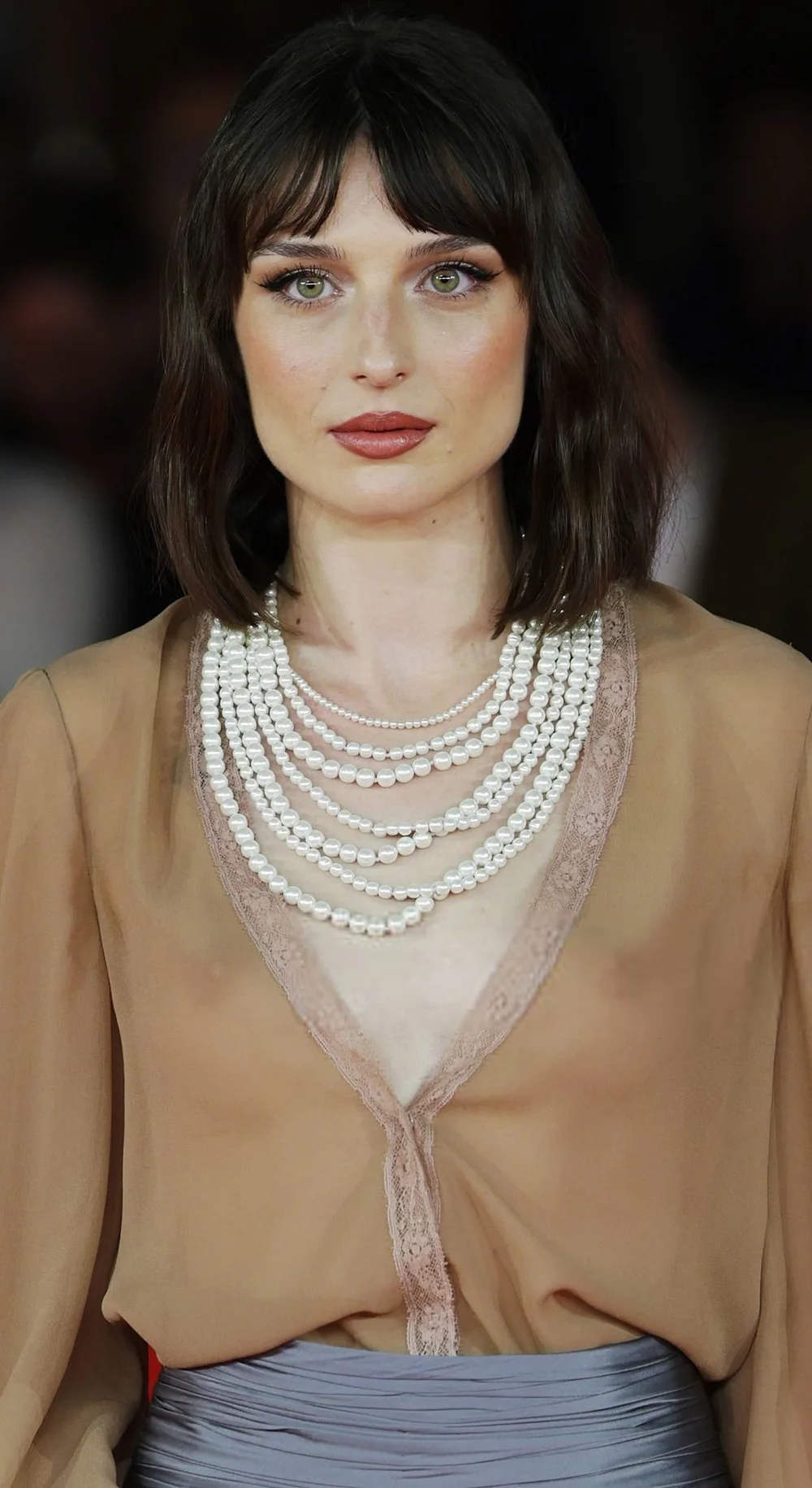 AlicePaganiSeeThroughLOraDiTuttiRomeFFPic2 A woman with dark hair wearing a multi-strand pearl necklace and a sheer tan V-neck top.