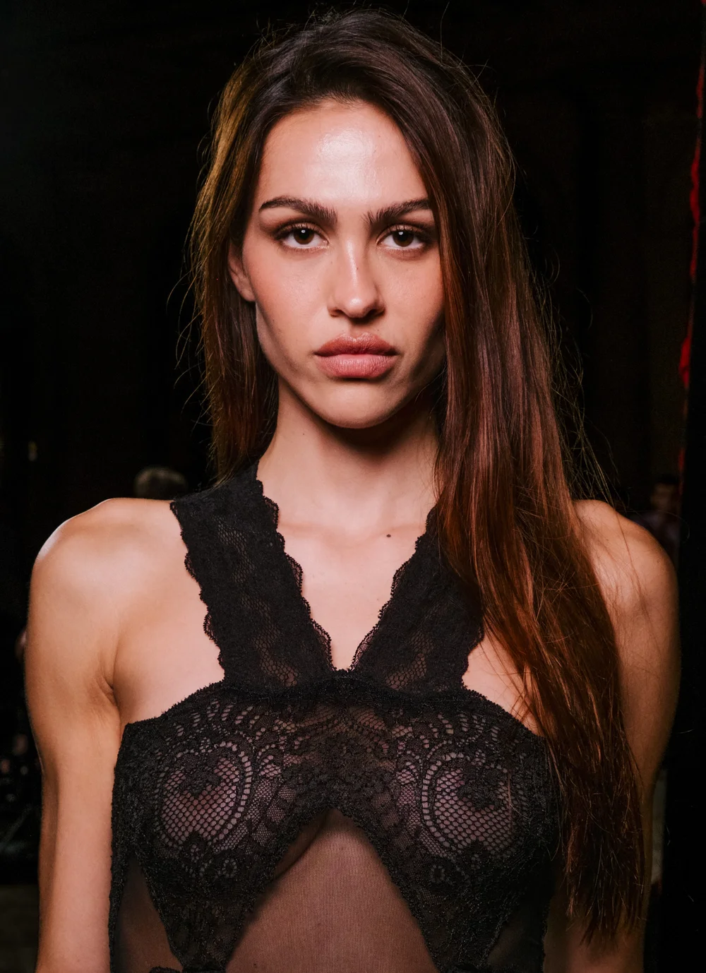 AmeliaGrayHamlinSeeThroughREVOLVELaunchParisPic1 A woman with long, dark hair wearing a black lace halter top looks toward the camera.