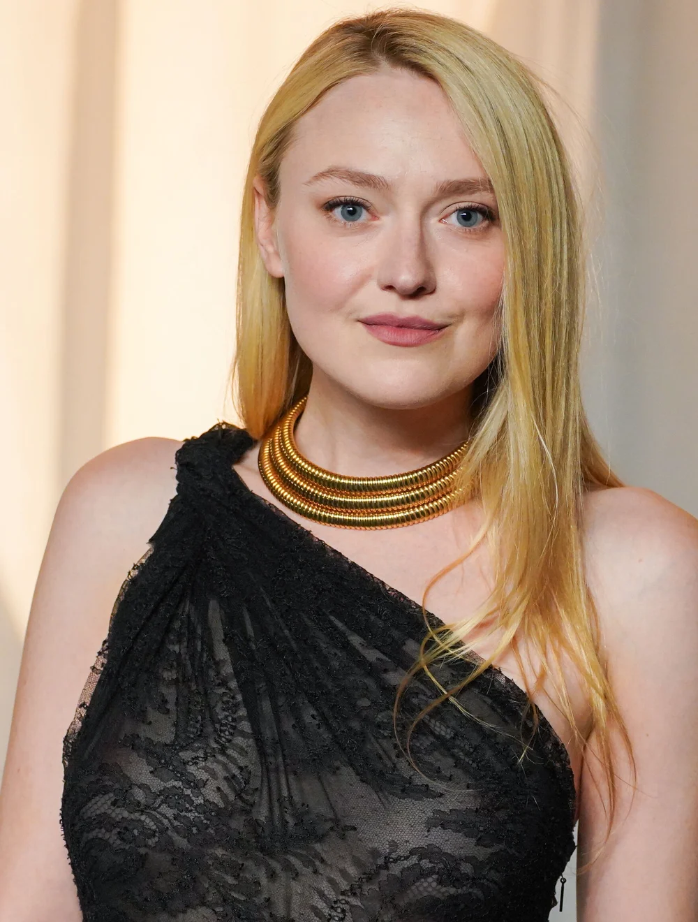 Dakota Fanning wearing a black lace one-shoulder dress and a thick gold-toned collar necklace.
