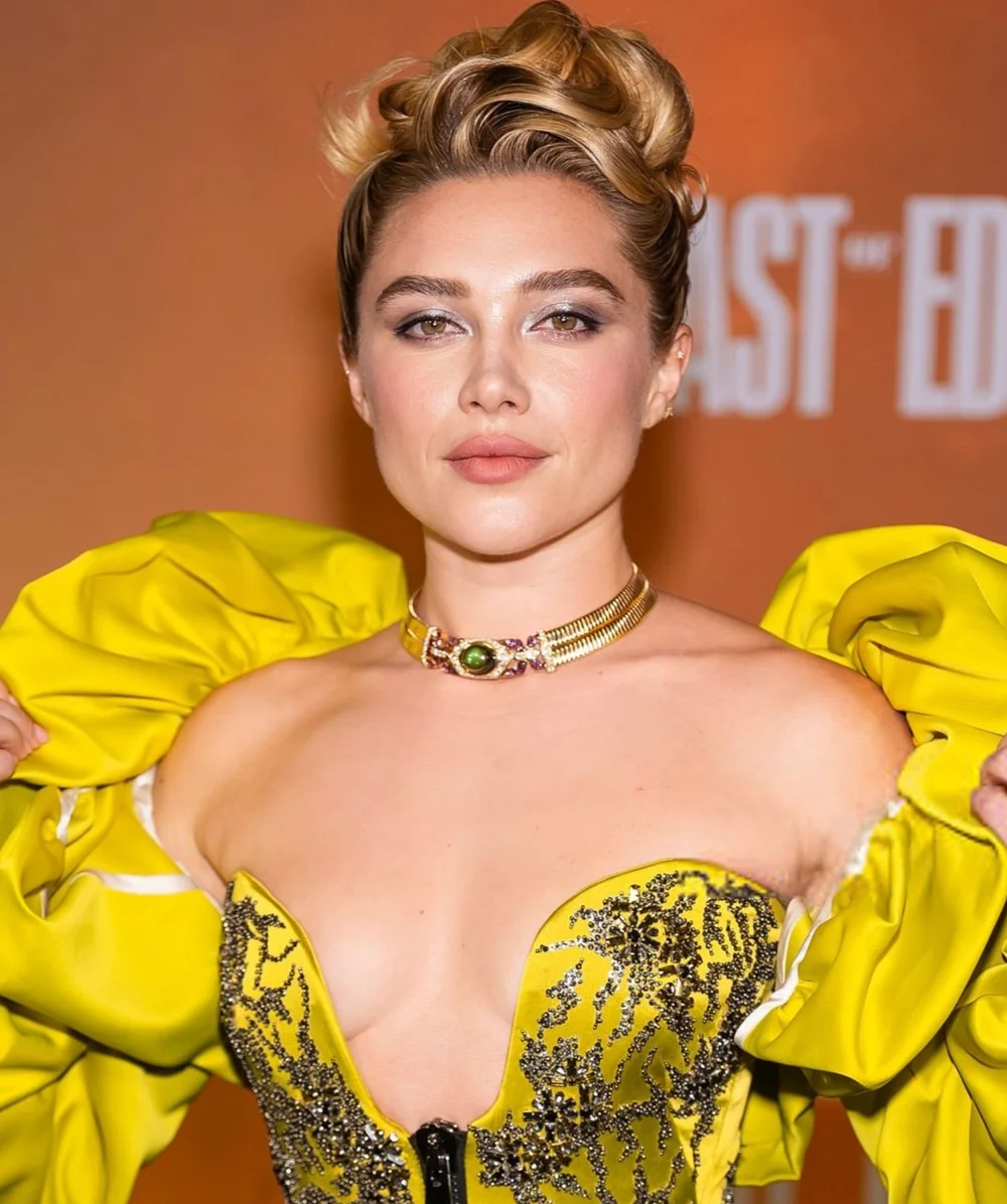 FlorencePughEastOfEdenPremNYCleavagePic1 Florence Pugh wearing an off-the-shoulder yellow dress with puffed sleeves and a gold choker necklace.