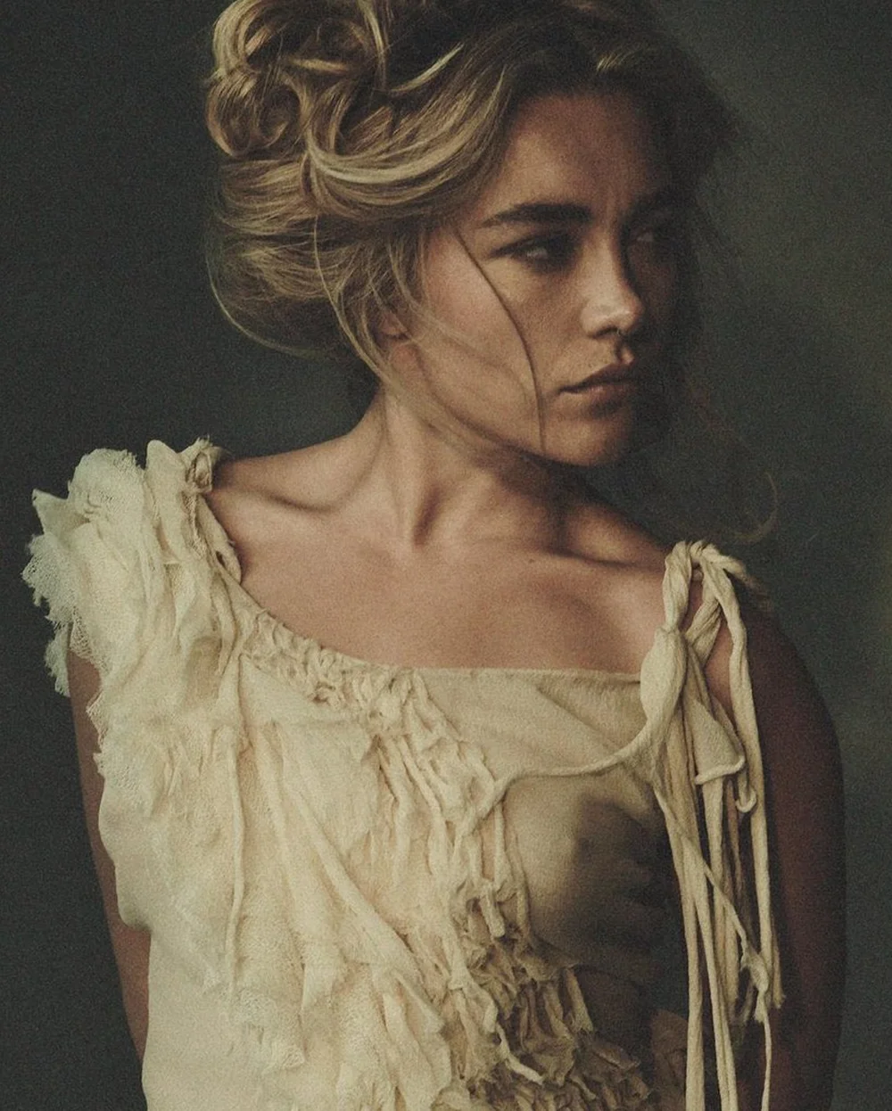 FlorencePughNetflixTudumPic1 A portrait of a woman with her hair in an updo, wearing a cream-colored top with frayed edges, looking toward the side.