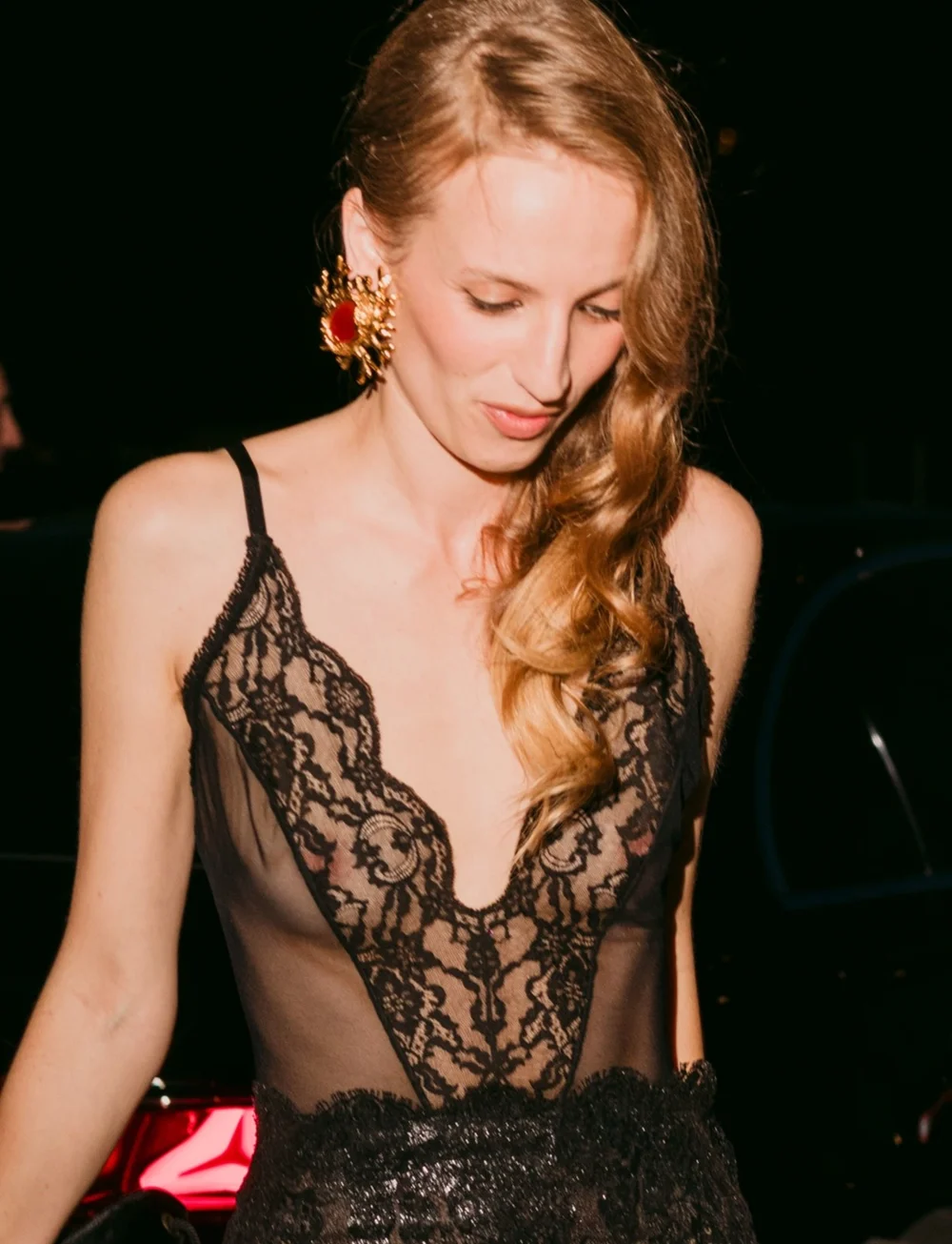 PetraCollins2026SaintLaurentFSPic1 A woman wearing a black lace camisole and a large, ornate red and gold earring.