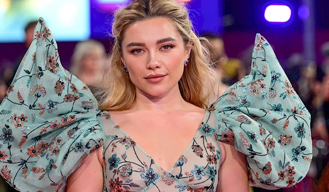 Florence Pugh wearing a sheer, light blue dress with oversized puffed shoulders decorated with floral embroidery.