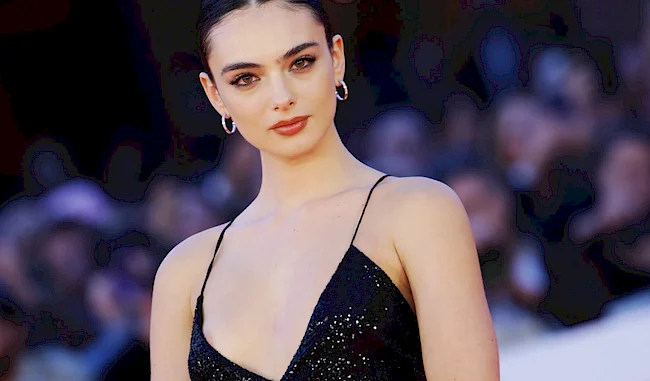 A woman wearing a black sequined dress and hoop earrings posing on a red carpet.