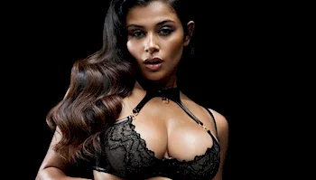 Indian woman with long dark hair wearing a black bra against a black background.