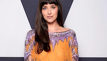Dakota Johnson posing in an orange dress with purple beaded fringe detail.