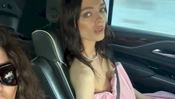 A woman wearing a pink garment sits in the passenger seat of a car, looking toward the camera.
