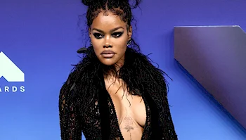 Teyana Taylor on a red carpet in front of a blue backdrop.