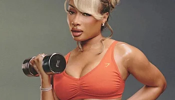 Megan Thee Stallion wearing an orange sports bra holding a metal dumbbell.