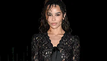 Zoë Kravitz wearing a black lace long-sleeved top against a black background.