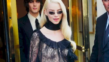 Anya Taylor-Joy wearing slim sunglasses and a black lace top, walking between two men in suits.