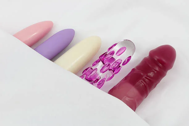 Five dildos of various colors and textures lined up against a white background.